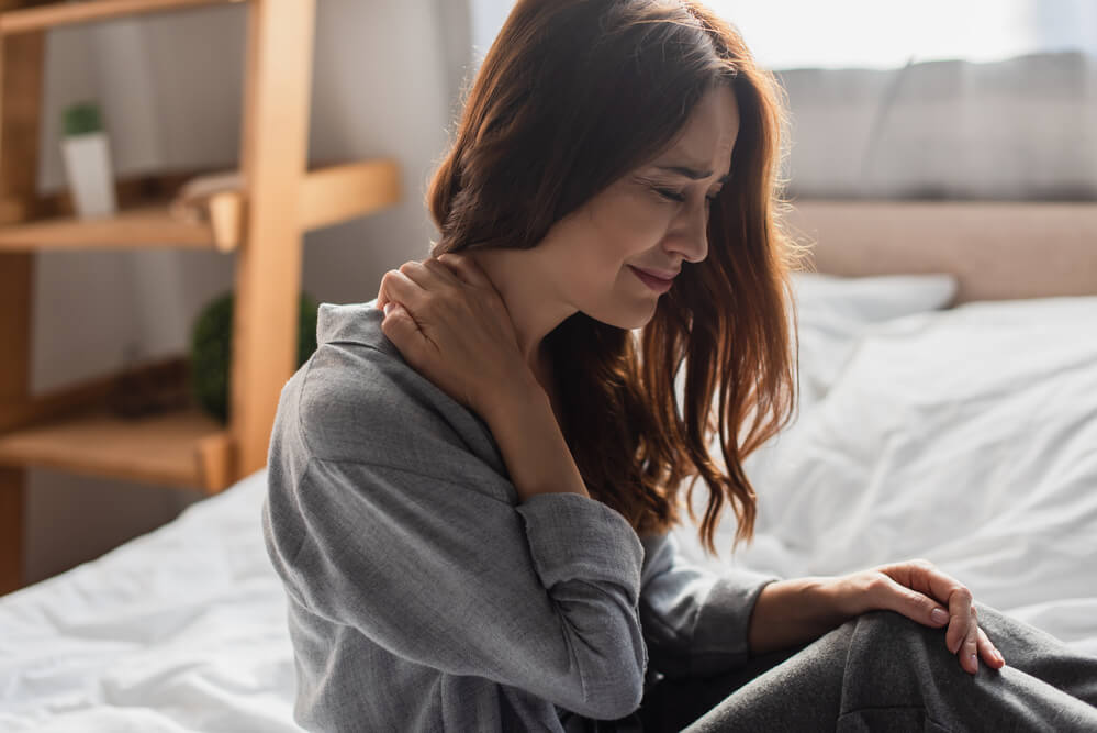 A wincing woman touches her neck. Pain and suffering may influence car accident settlements.