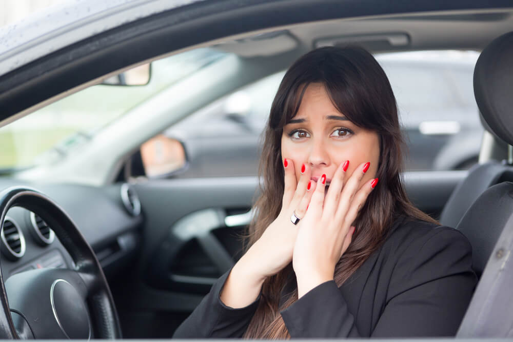 A woman in a car covers her mouth in shock. 